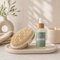 Bottle of 'The Ascent' body oil with a brush on a tray, set against a neutral background.