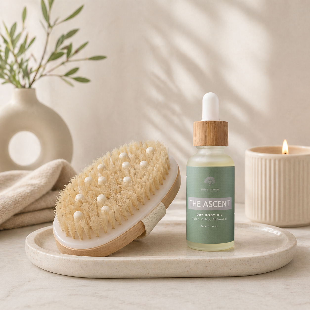 Bottle of 'The Ascent' body oil with a brush on a tray, set against a neutral background.