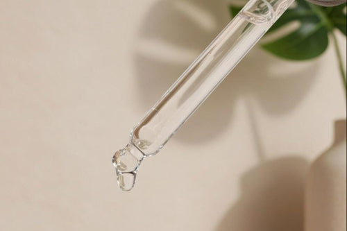Glass dropper with a drop of liquid over a light-colored wall and wooden surface.